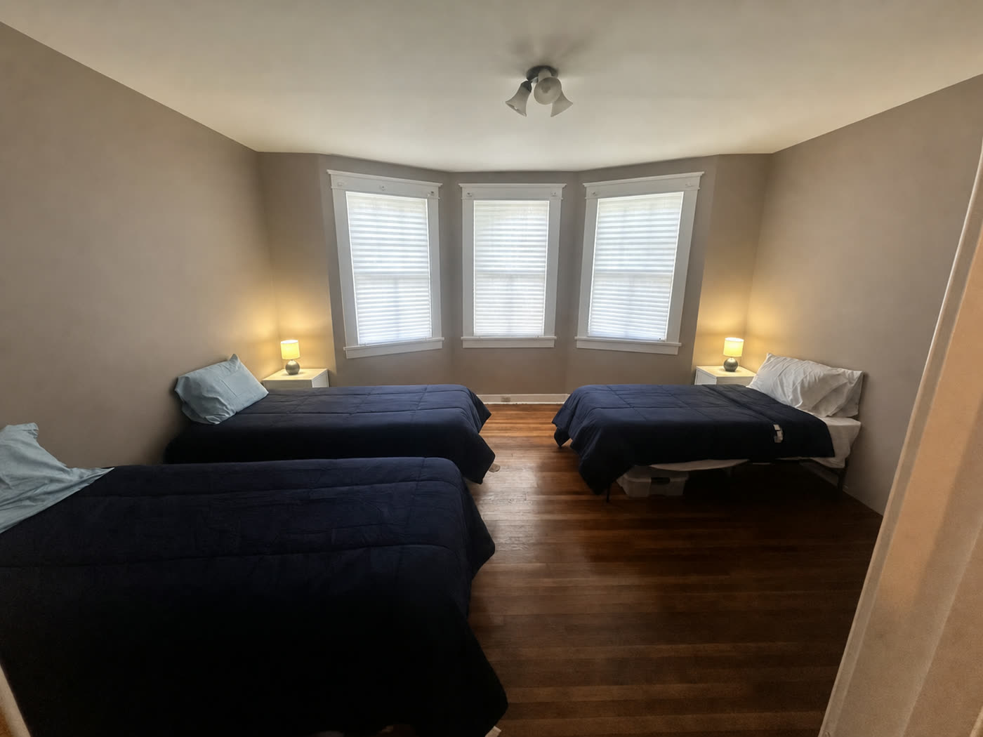 A bright, comfortable shared bedroom with three beds and a bay window